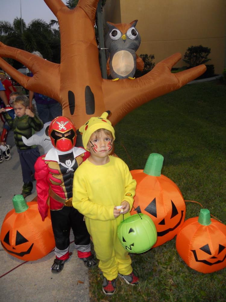Child dressed as red Power Ranger and kid dressed as Pikachu standing in front of inflatable Halloween tree and inflatable jack-o-lanterns